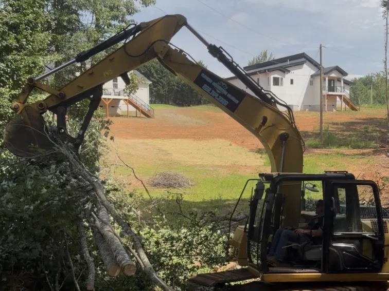 Excavator lifting cut timber during land clearing on a residential property in the Hickory, NC area