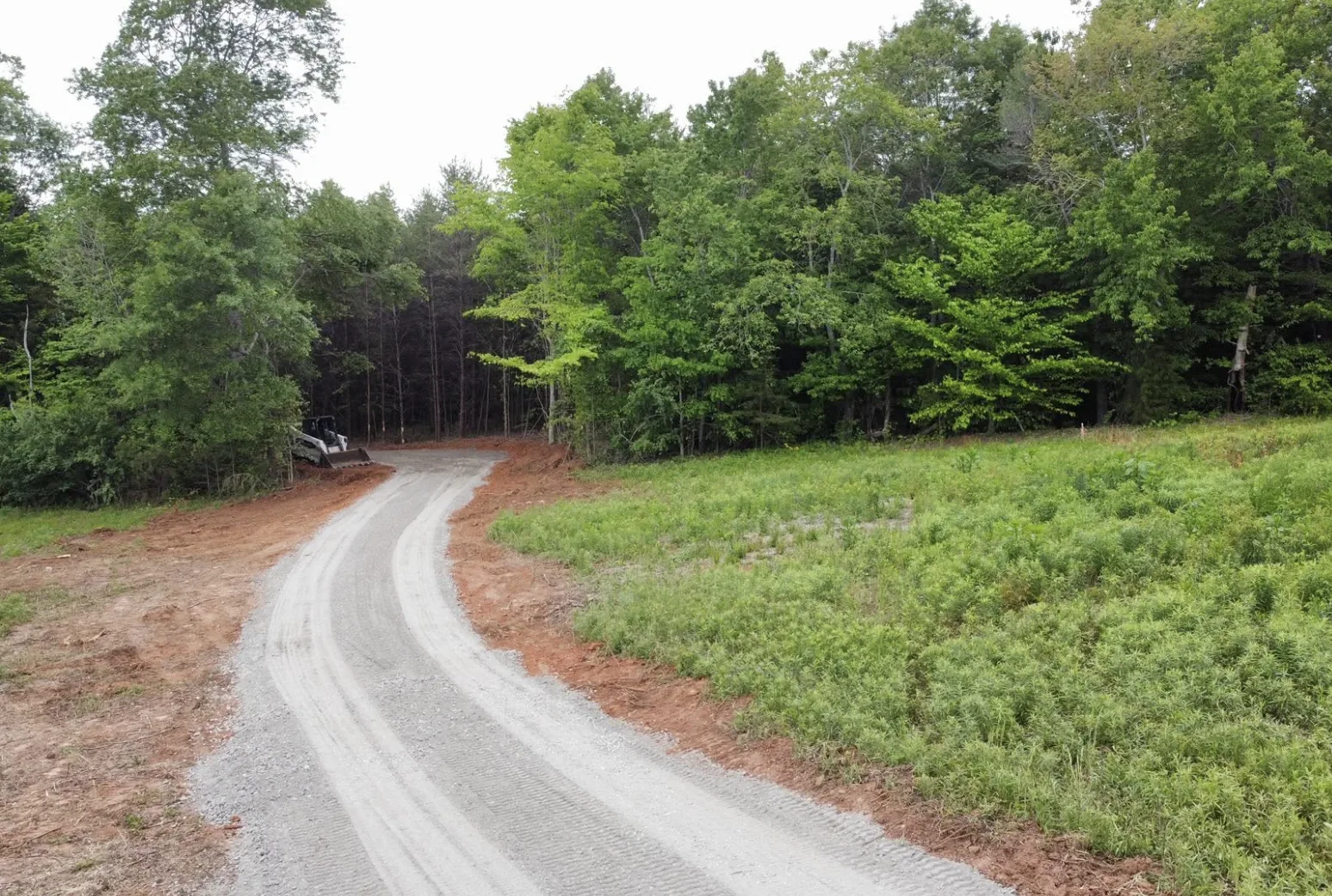 New gravel access road graded through a green clearing